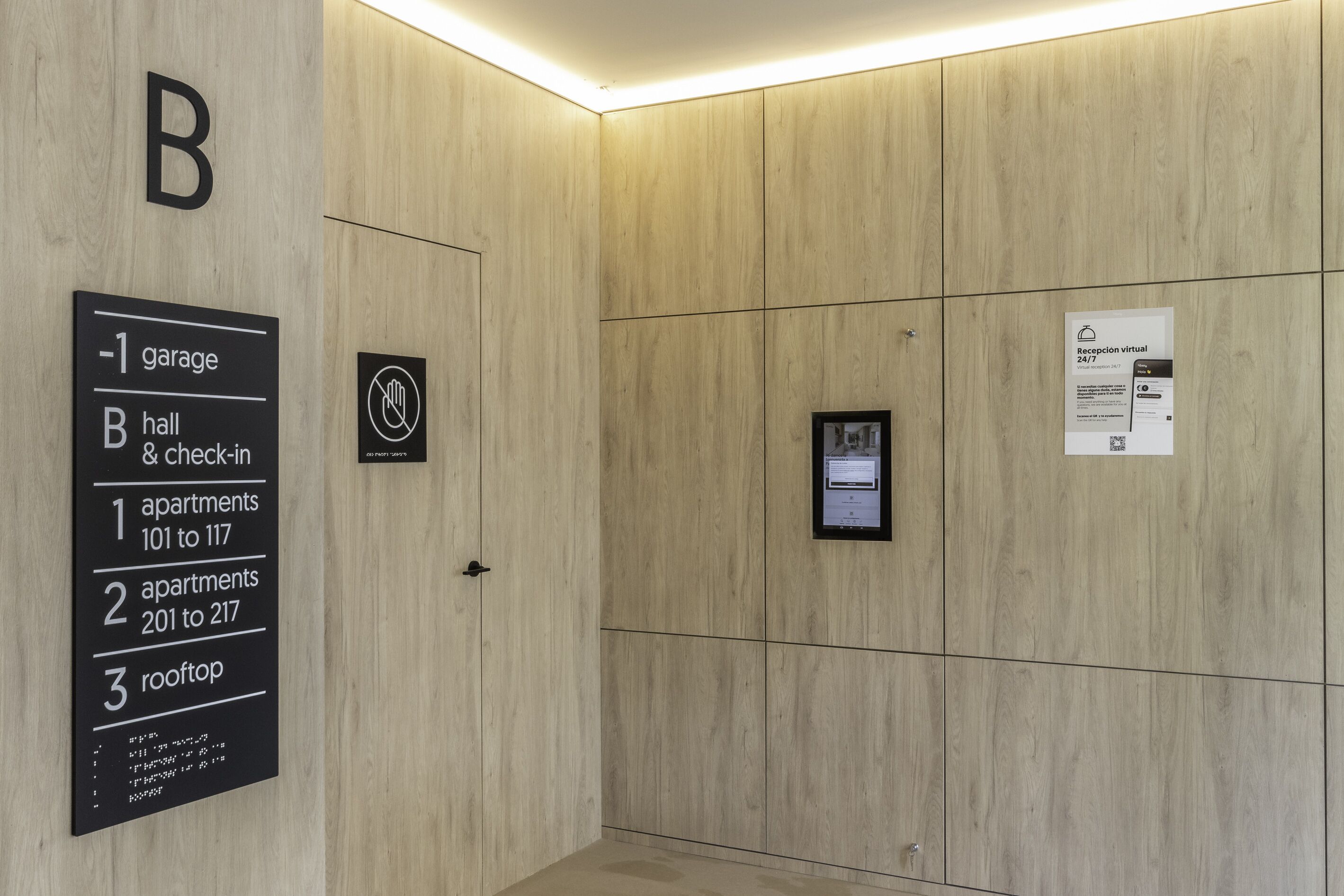 L’intérieur d’un hôtel avec un mur revêtu de panneaux de bois, un panneau indiquant l’emplacement du garage, du hall et de la réception, ainsi que les appartements 101 à 117, les appartements 201 à 217 et la terrasse sur le toit.