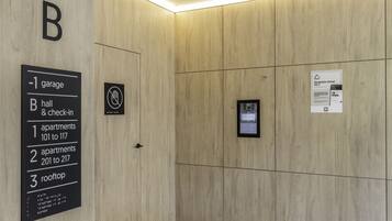 L’intérieur d’un hôtel avec un mur revêtu de panneaux de bois, un panneau indiquant l’emplacement du garage, du hall et de la réception, ainsi que les appartements 101 à 117, les appartements 201 à 217 et la terrasse sur le toit.