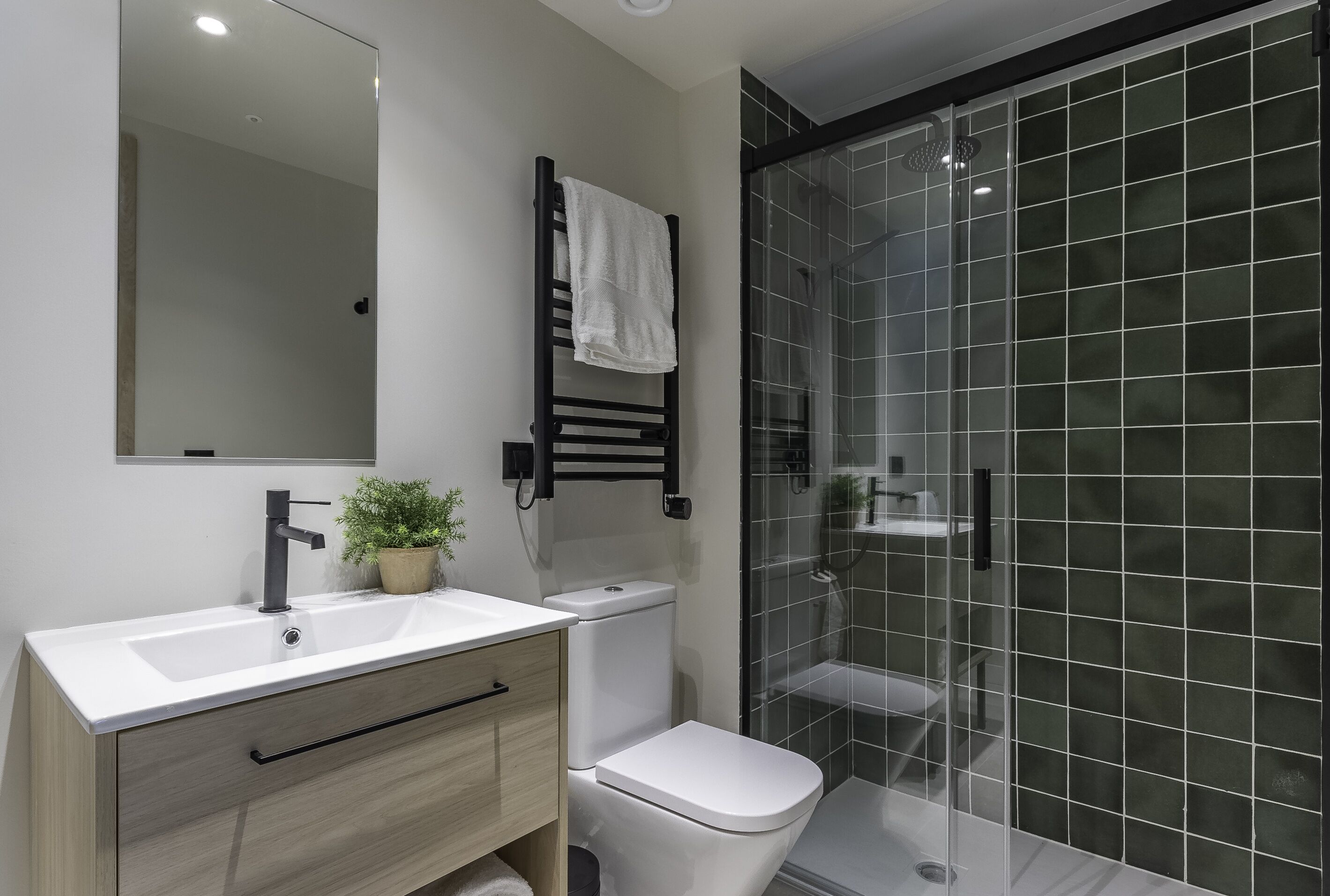 A bathroom with a white sink, a black towel rack, a white toilet, and a glass shower enclosure.