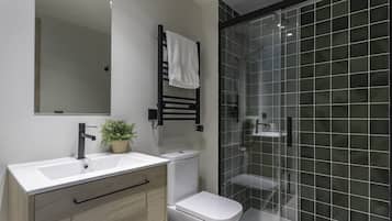 A bathroom with a white sink, a black towel rack, a white toilet, and a glass shower enclosure.