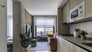 A modern kitchen with a built-in microwave, a dining area with a table and chairs, a sofa, and a large window offering a view of buildings. - Líbere Pamplona Yamaguchi (Pamplona)