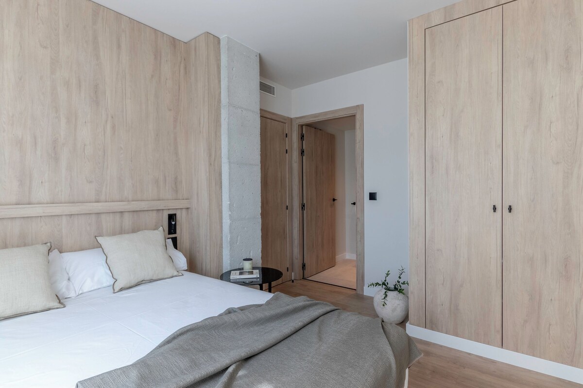 A bedroom with a large bed, wooden wardrobe, and a small bedside table with a lamp.