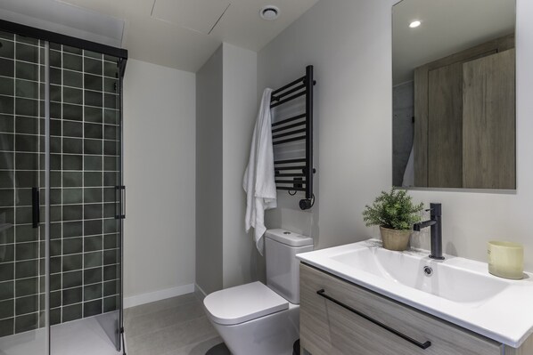 A modern bathroom with a glass shower enclosure, a white toilet, a towel rack, a sink with a mirror, and a potted plant. - Líbere Pamplona Yamaguchi (Pamplona)