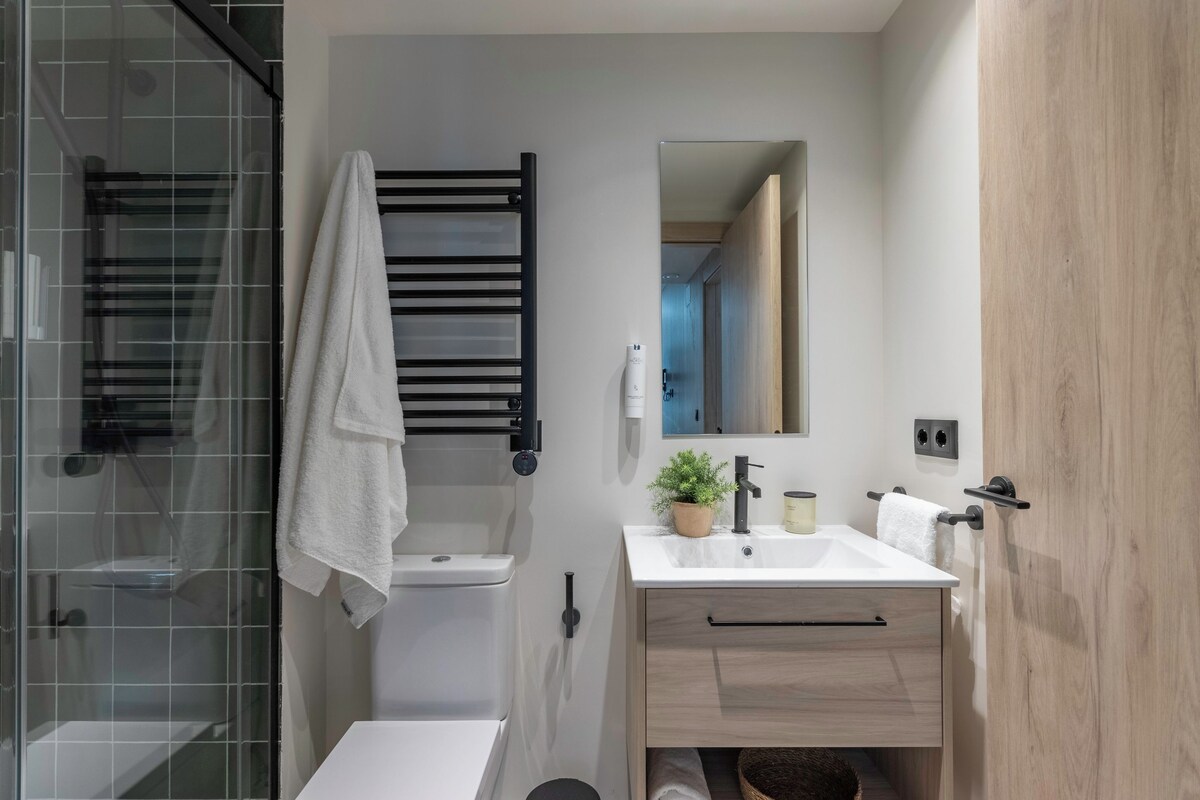 A modern bathroom with a glass shower enclosure, a white sink, a mirror, and a wooden vanity.