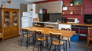 A compact kitchen with a dining area, wooden cabinets, a refrigerator, microwave, and a coffee maker. - Welcome to Genets du Sancy (BESSE-ET-SAINT-ANASTAISE)