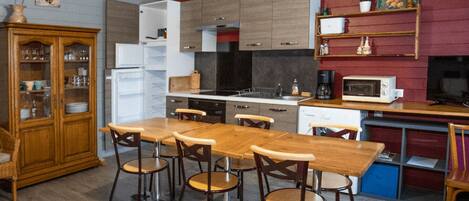 Una cocina compacta con comedor, muebles de madera, refrigerador, microondas y cafetera.