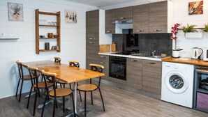 Una cucina moderna con mobili in legno, forno a incasso, lavastoviglie e zona pranzo con tavolo e sedie in legno.