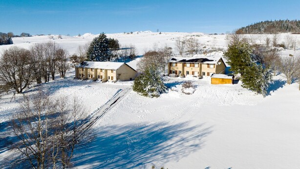 Paesaggio innevato con due edifici, uno dotato di un ampio garage, circondati da alberi e campi aperti.