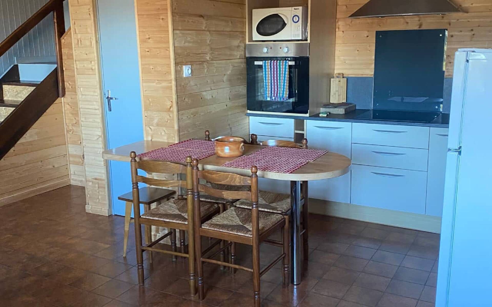 A kitchen with a wooden table, chairs, a microwave, oven, and a refrigerator.