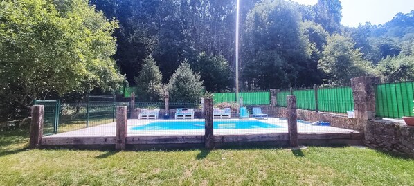 Piscina exterior con valla, sillas de descanso y pared de piedra.