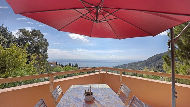 A balcony with a table, chairs, a red umbrella, and a view of the sea. - Pet-Friendly Apartment 'La Colombera' with Sea View, Garden & Wi-Fi (Alassio)
