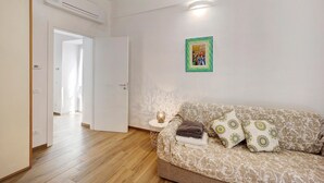 A living room with a sofa, pillows, a small table with a lamp, and a framed picture on the wall. - Pet-Friendly Apartment 'La Colombera' with Sea View, Garden & Wi-Fi (Alassio)