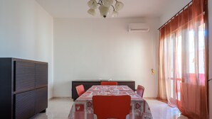 Un comedor con una mesa preparada para cuatro personas, un mueble de color oscuro y un ventanal con cortinas translúcidas.