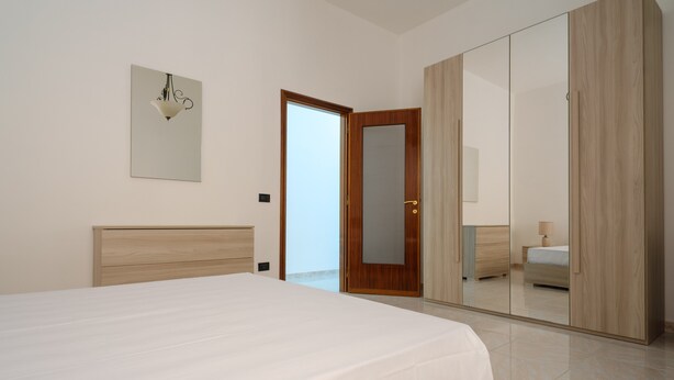 Un dormitorio con cama, armario de madera, espejo y lámpara de pared.