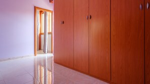 Un pasillo con armarios de madera, suelo de baldosas y un acceso a otra habitación.