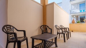 Un balcón con una mesa y sillas, una pared color crema y un edificio con balcones al fondo.