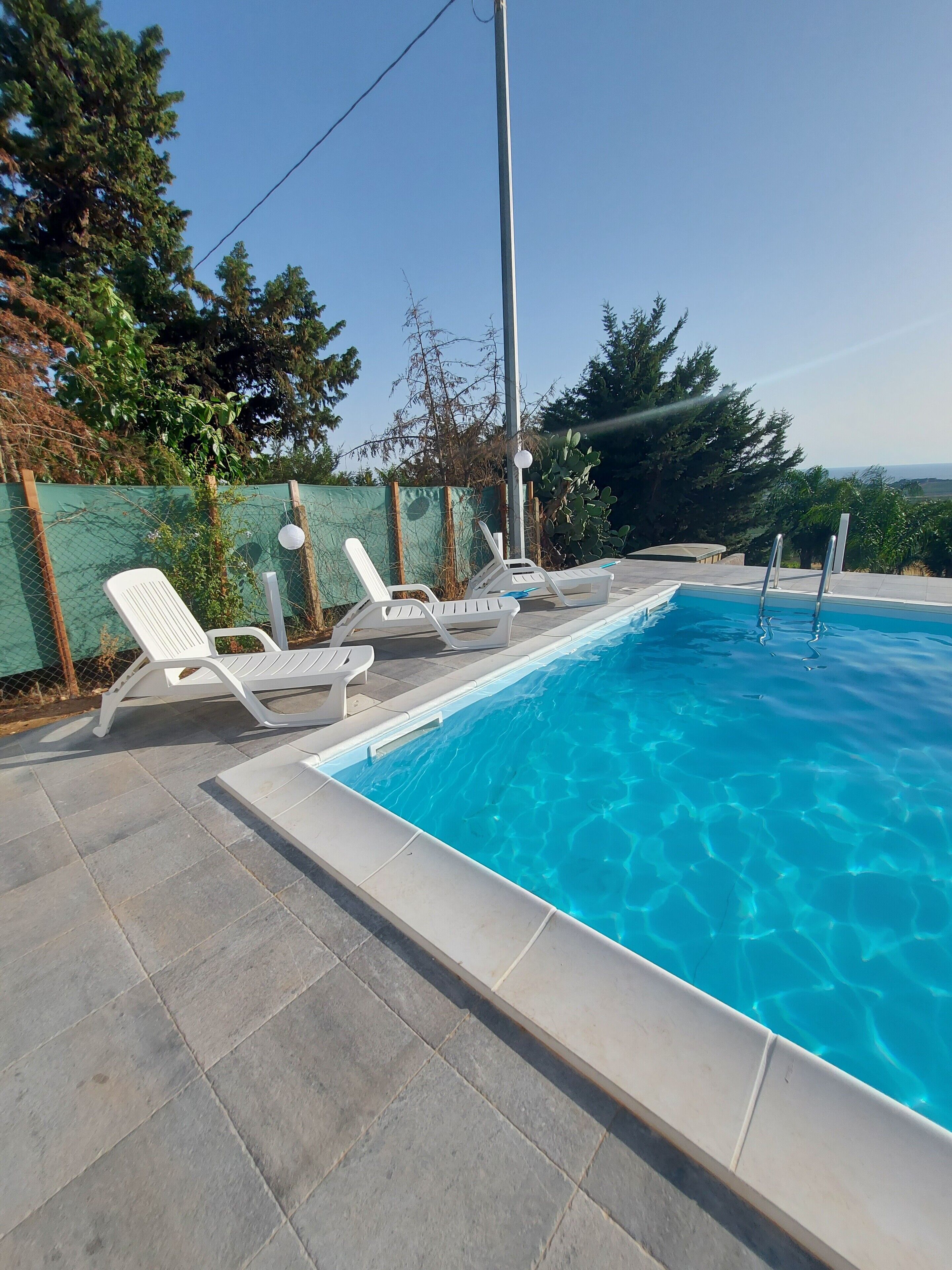 Una piscina rettangolare con acqua cristallina e azzurra, circondata da un solarium piastrellato.