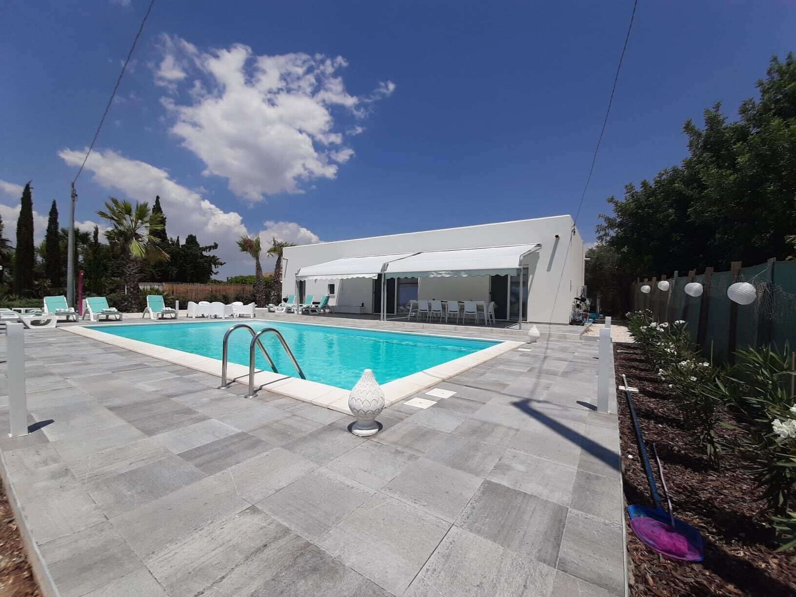 A swimming pool with lounge chairs, a covered seating area, and a building with a white facade.