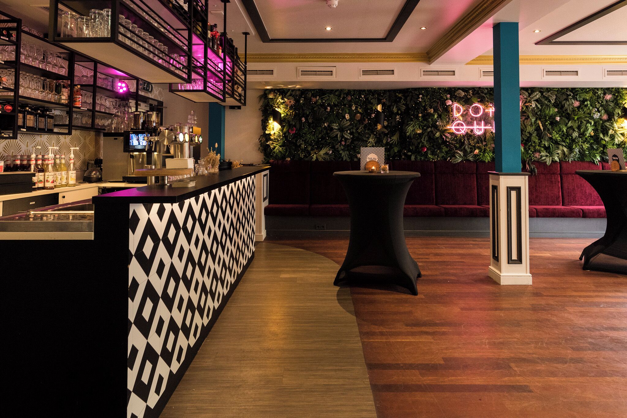 Eine Bar mit Regalen voller Gläser und Flaschen, einem Neonlichtschild und einem Holzboden.