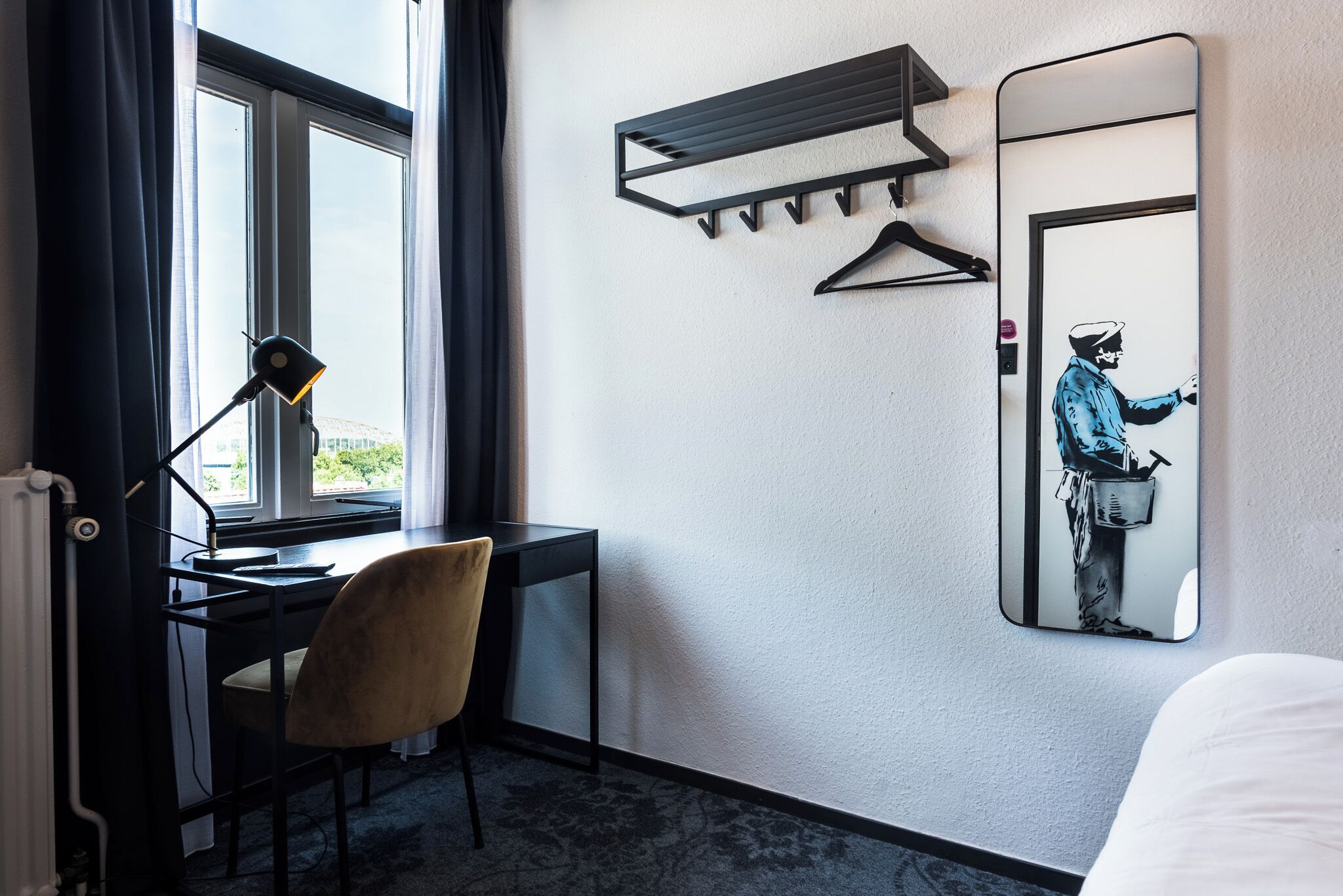 Habitación de hotel con escritorio, silla y un espejo grande con un cuadro.