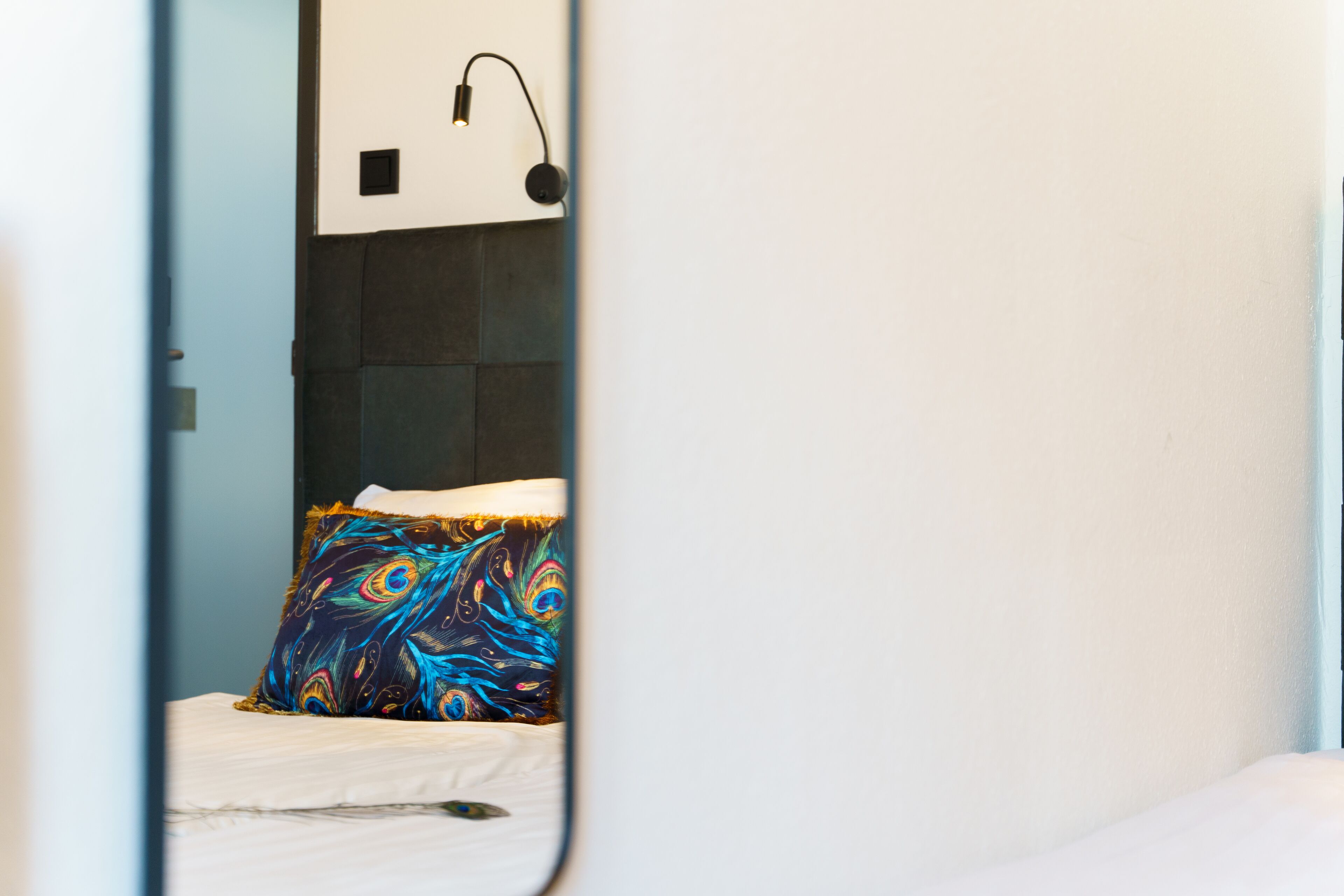 A bedroom with a bed, a colorful pillow, a wall-mounted light, and a dark-colored headboard.