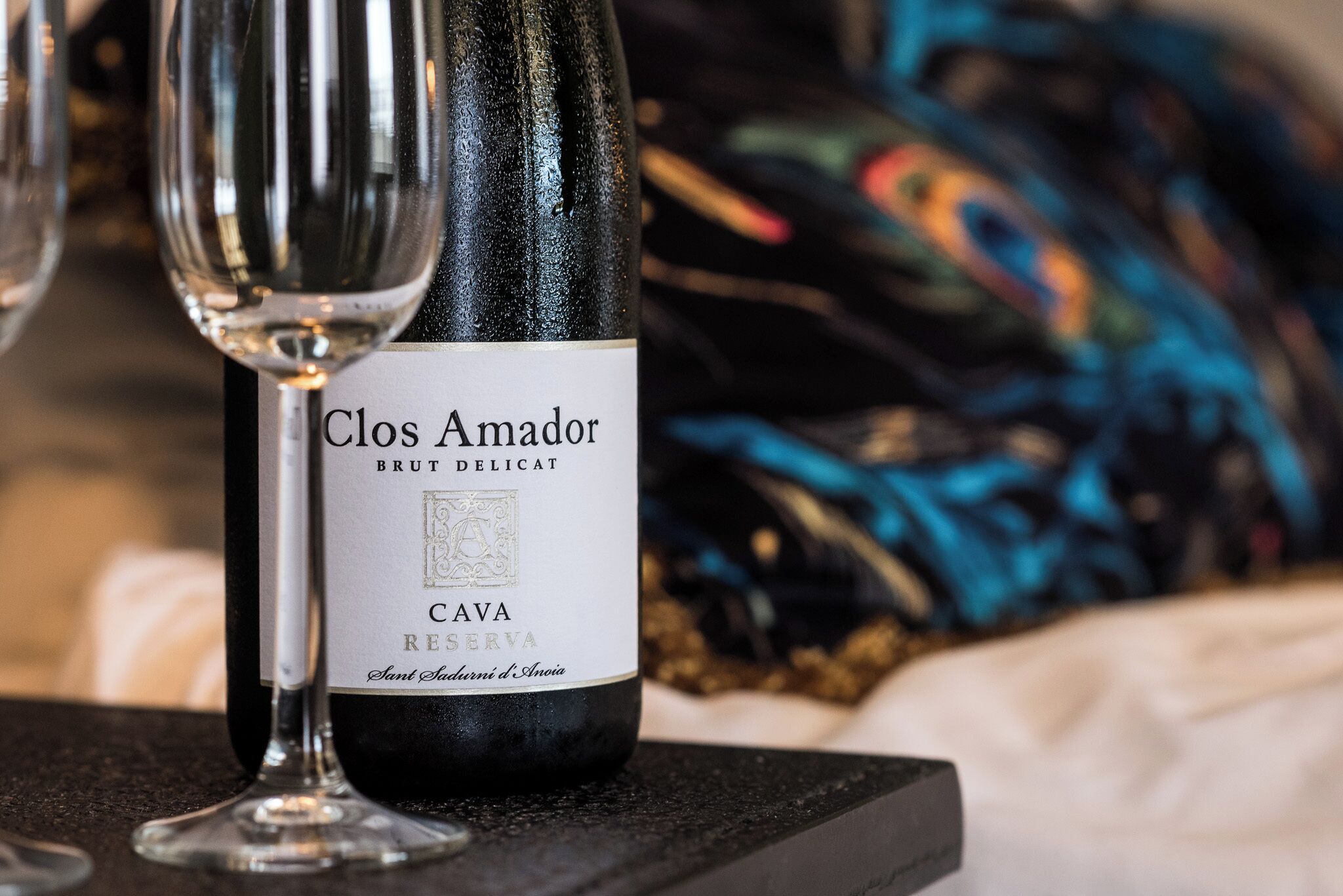 A bottle of Clos Amador Brut Delicat Cava Reserva on a table with a glass.