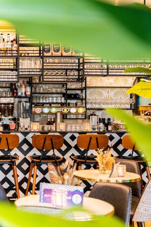 A bar area with shelves of bottles and glasses, wooden chairs, and a patterned wall. - Hotel Pauw (Nijmegen)