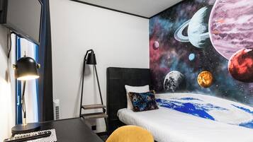 Ein Hotelzimmer mit Bett, Schreibtisch, Stuhl und einer Wandmalerei von Planeten.