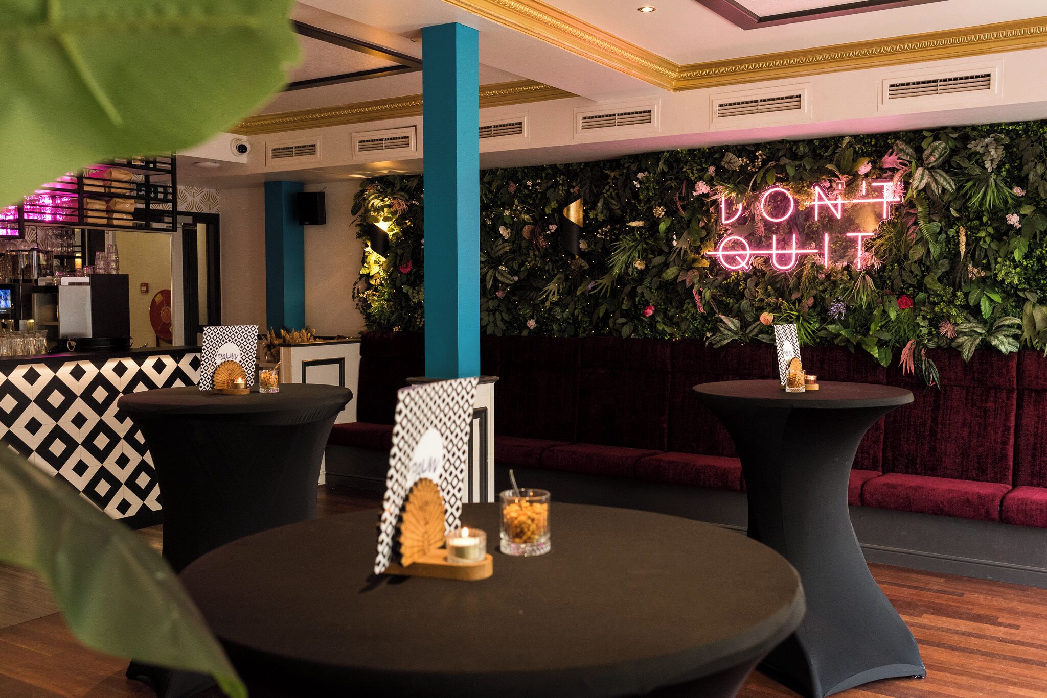 A modern bar area with two round tables, a neon sign, and a lush green wall.