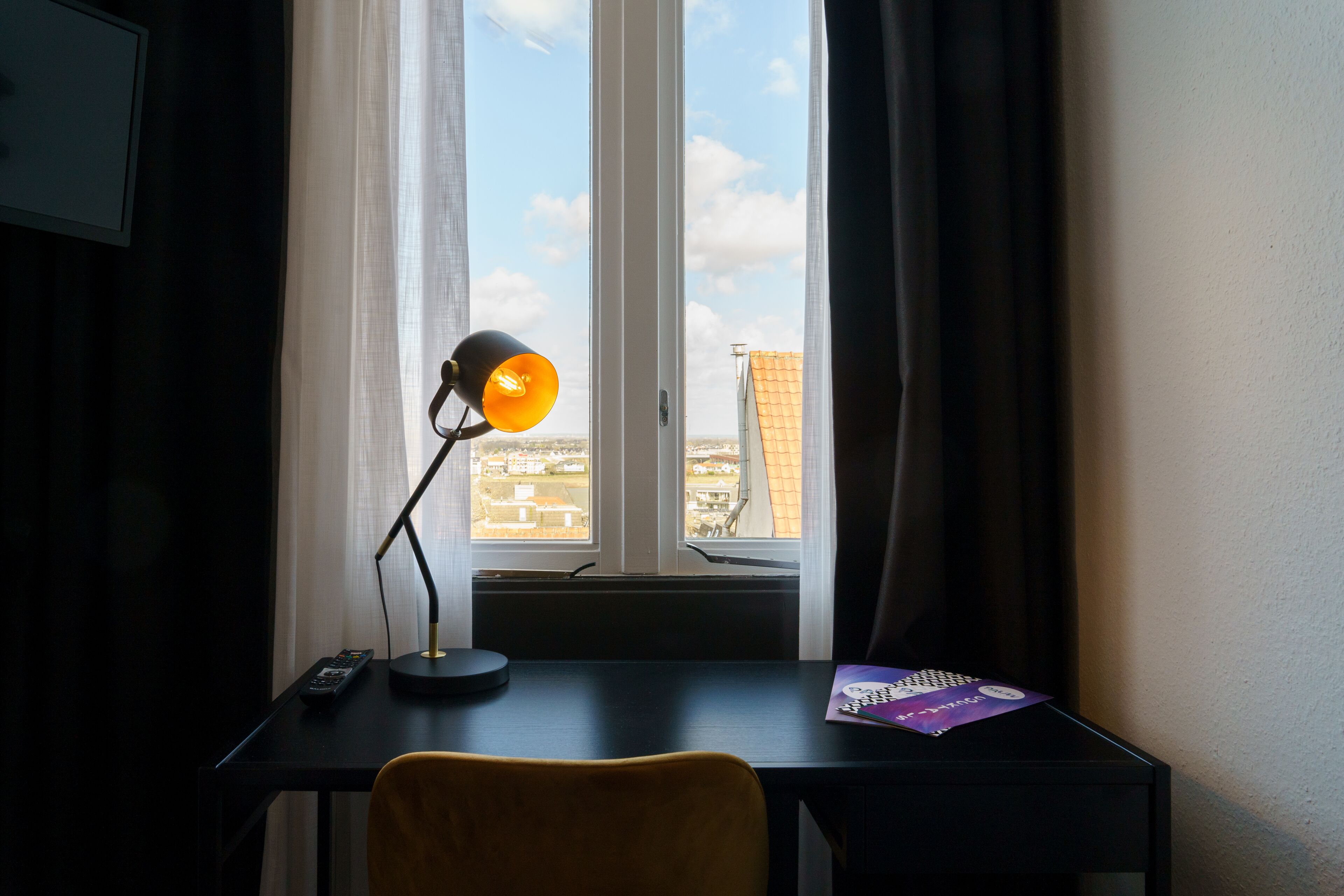 A room with a desk, a lamp, a chair, and a window with curtains.