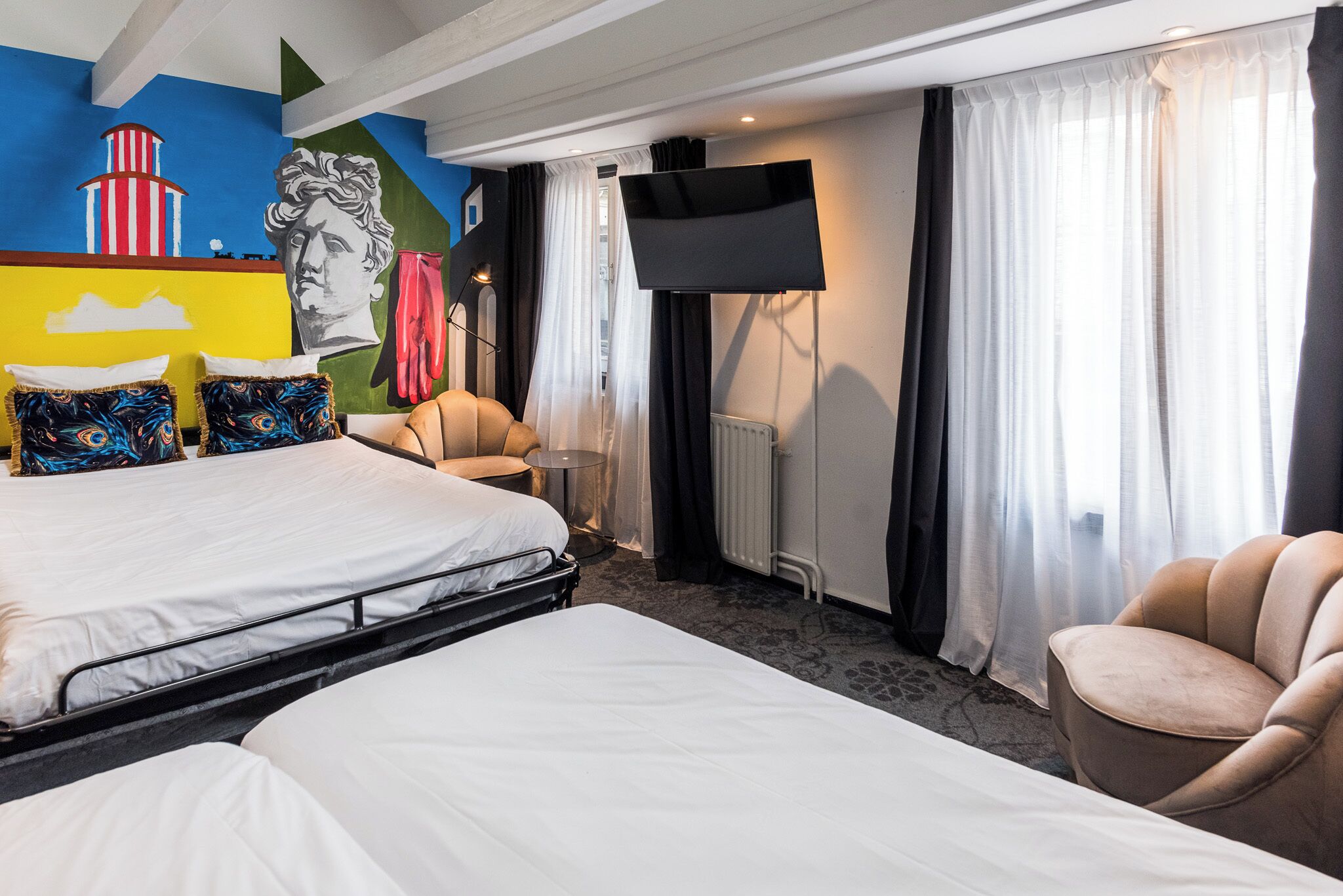 Habitación de hotel con dos camas, un televisor de pantalla plana, una silla y un mural en la pared.