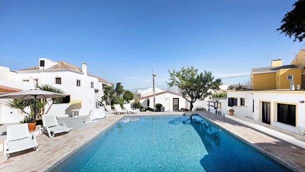 Une piscine avec des chaises longues, une pergola et un ciel d’un bleu limpide.
