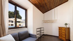Une pièce comprenant un canapé, une commode en bois, un étagère en métal et une fenêtre donnant sur des arbres et des bâtiments.