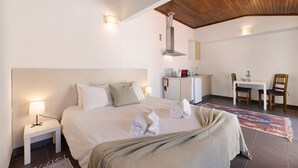 Une chambre d’hôtel comprenant un lit, une table de chevet, une lampe, des serviettes, un bureau avec des chaises et un coin cuisine.