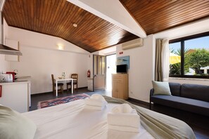 Habitación de hotel con cama, sofá, escritorio con silla, televisor y ventana con cortinas.