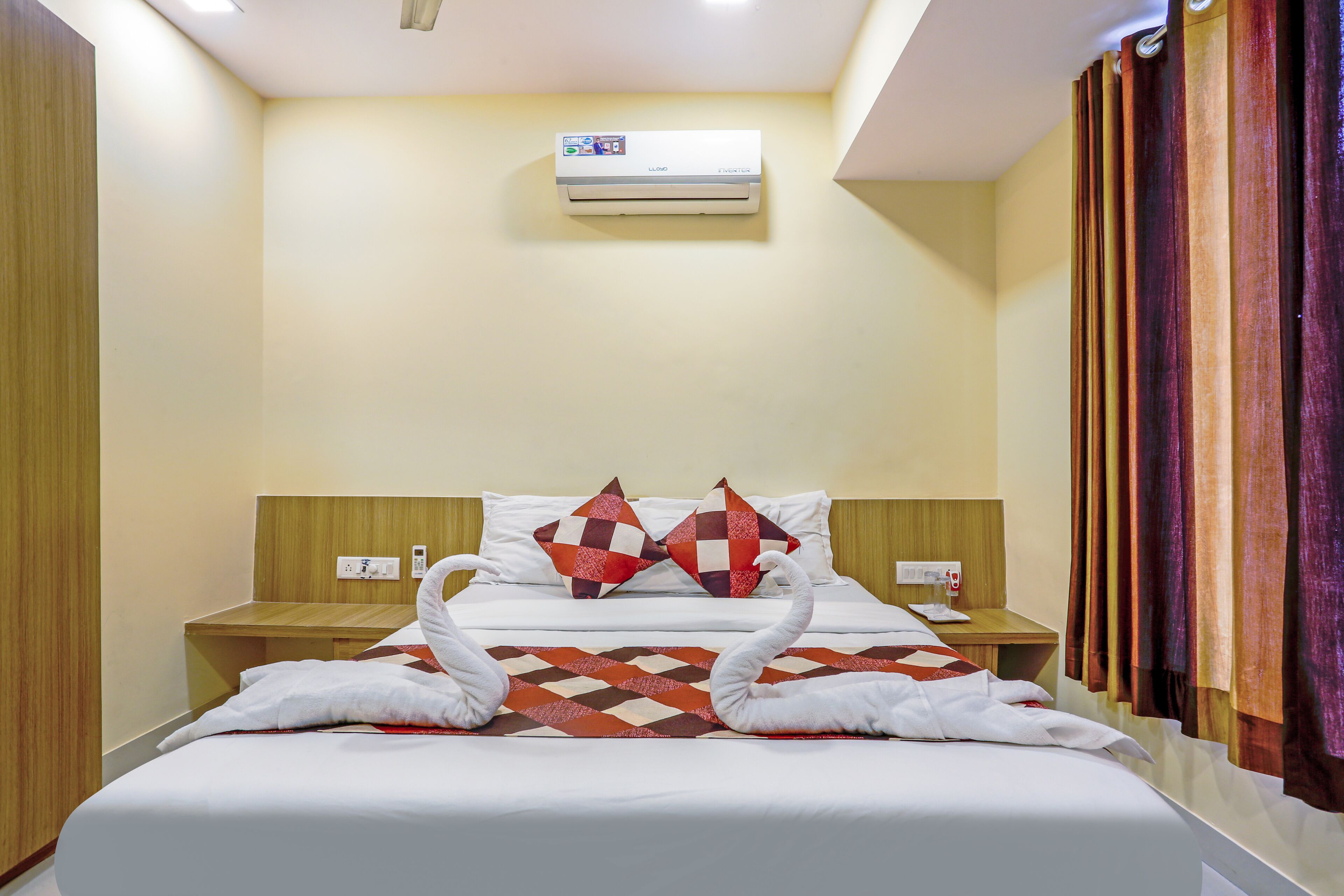 A hotel room with a bed, two nightstands, an air conditioning unit, and a curtain.