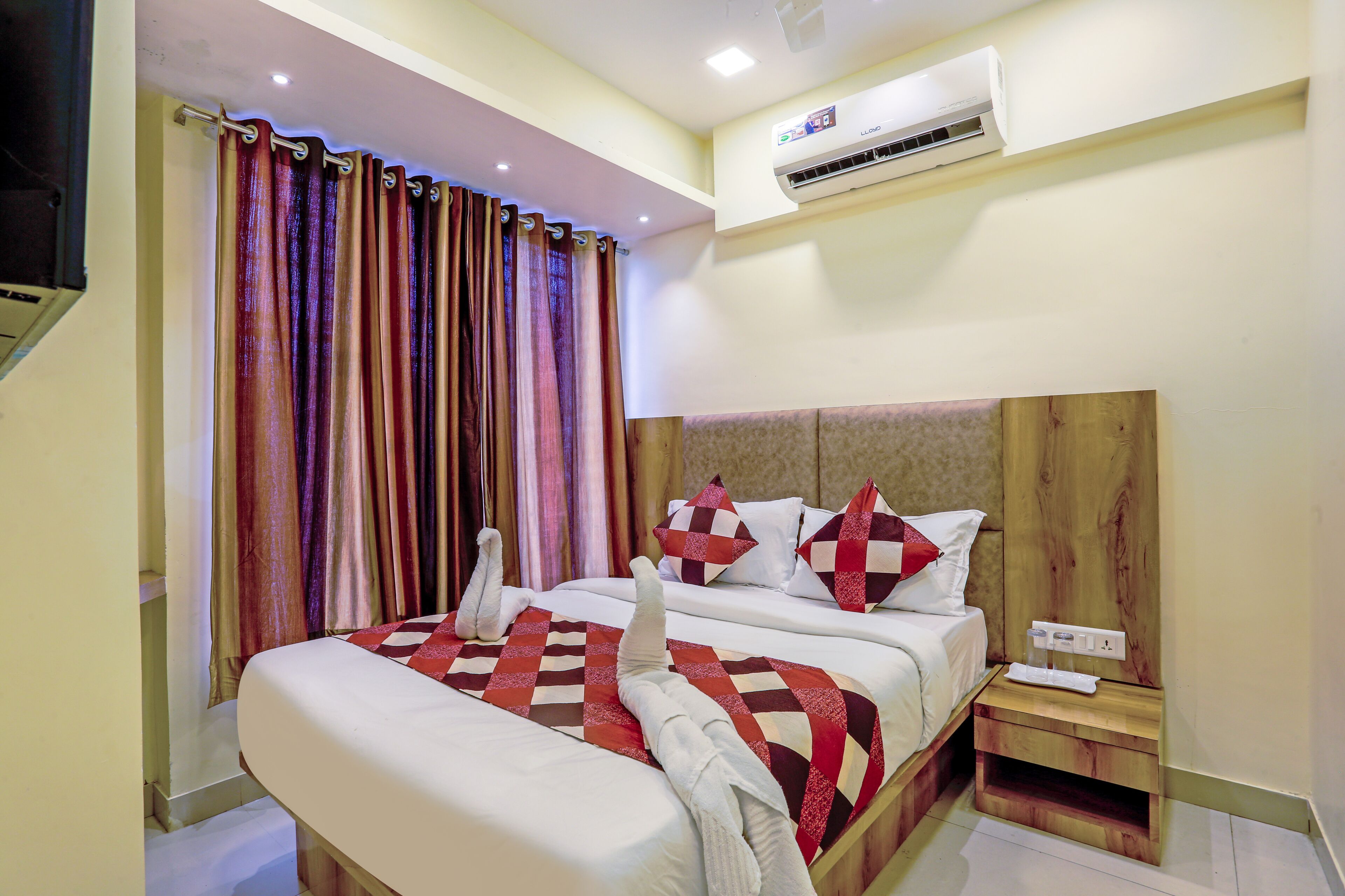 A hotel room with a bed, a nightstand, an air conditioner, and a curtain.