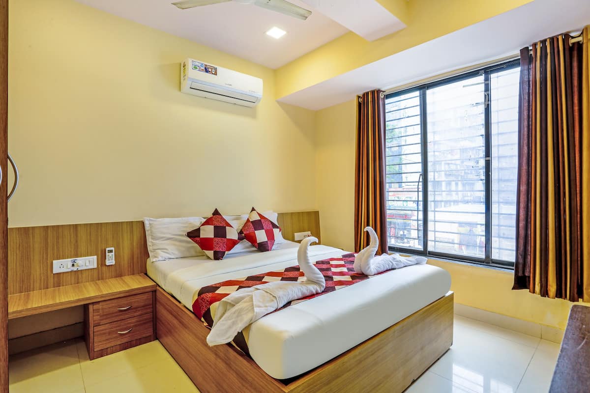 A hotel room with a bed, bedside table, and a window with curtains.