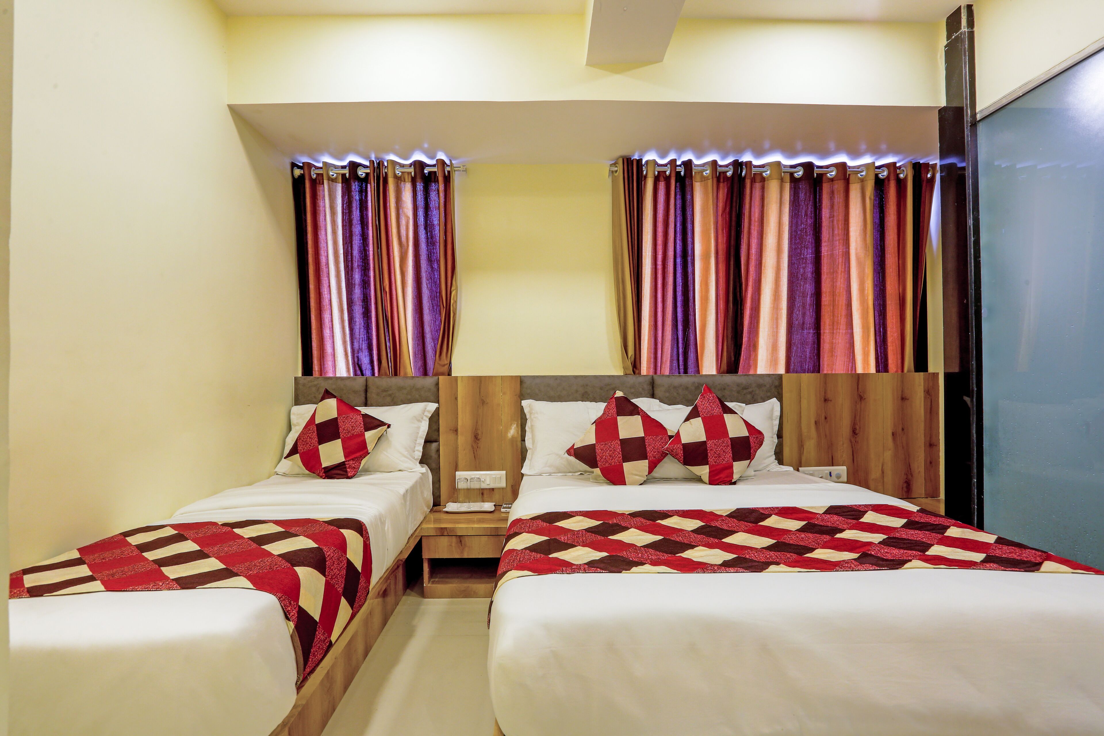 A hotel room with two beds, each with a wooden headboard, white bedding, and red and white checkered blankets.