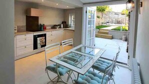 A modern kitchen with white cabinets, a glass dining table, and blue cushioned chairs.