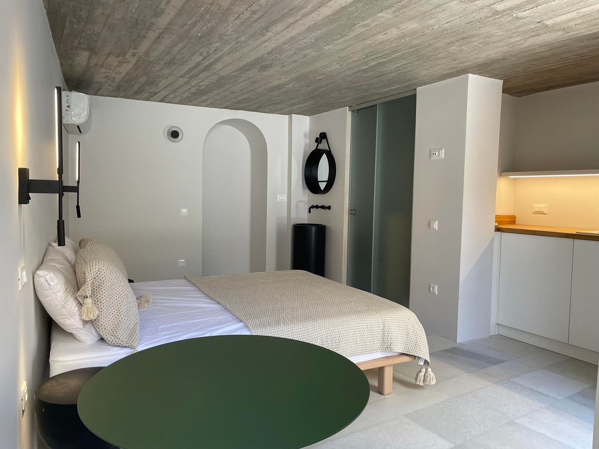 Een moderne slaapkamer met een bed, een klein rond tafeltje, een spiegel en een badkamer met douche.