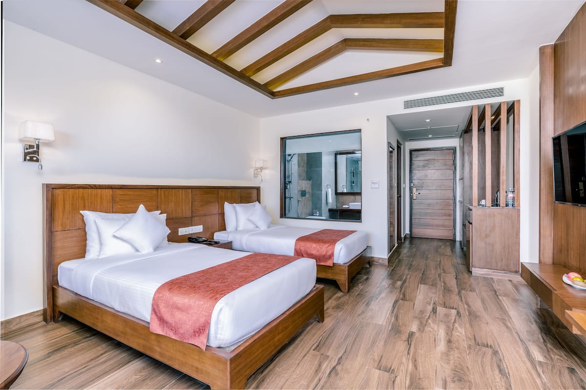 Habitación de hotel con dos camas, cabeceros de madera, ropa de cama blanca, un espejo grande y piso de madera.