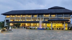 Un hotel con un edificio amplio de varios pisos, una fuente en el patio y una zona cubierta con luces.