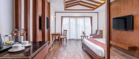A hotel room with a bed, a TV, a desk with a chair, a window with curtains, and a wooden ceiling design.