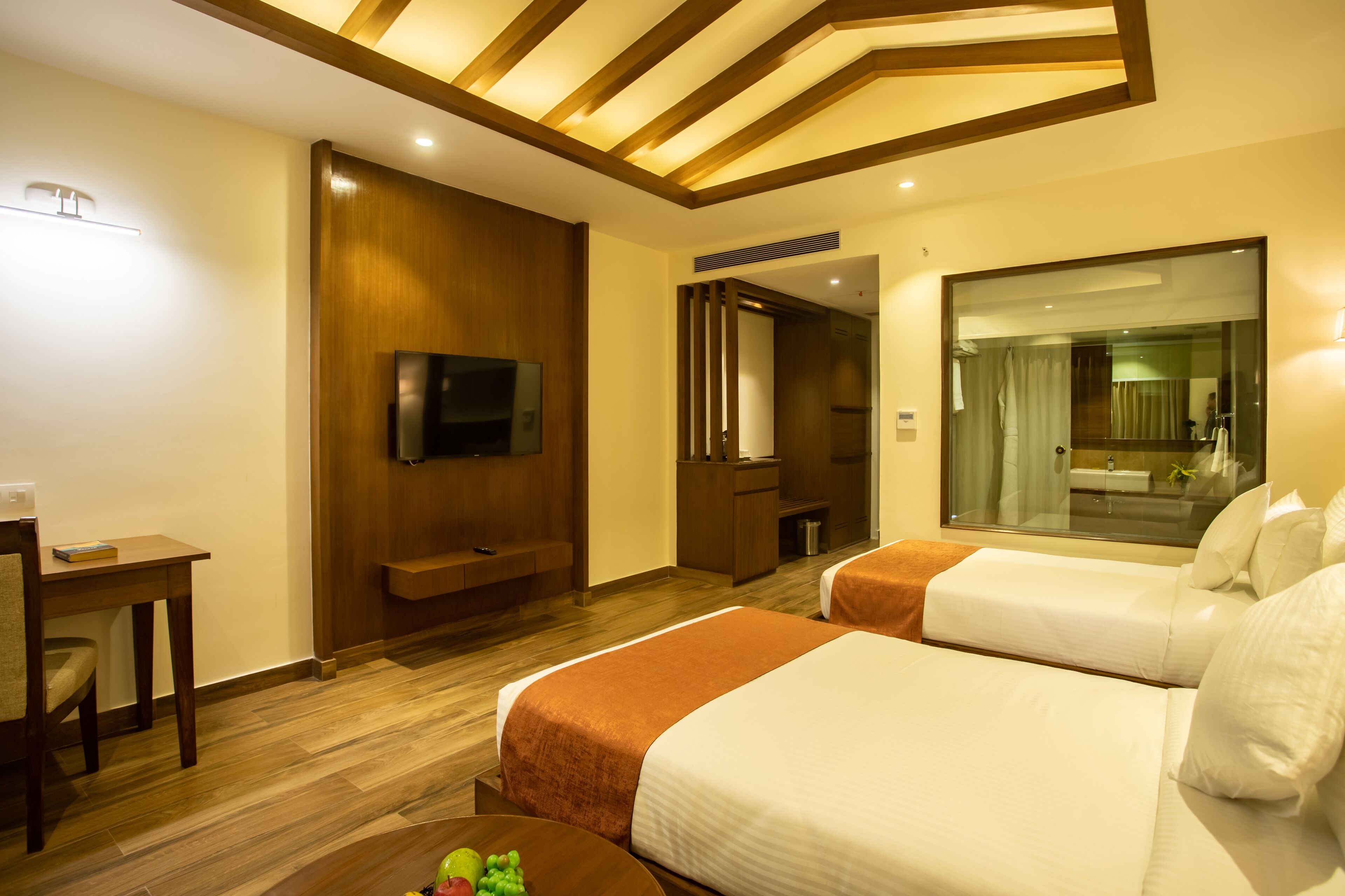 A hotel room with two beds, a TV, a desk, and a mirror.