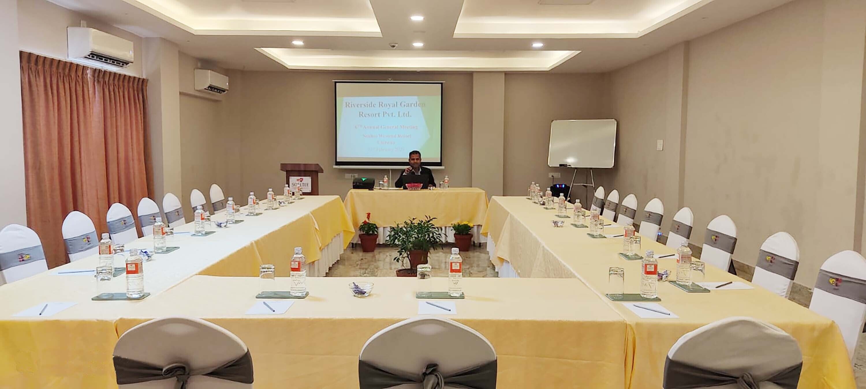 A conference room with a long table, chairs, a podium, and a presentation screen.