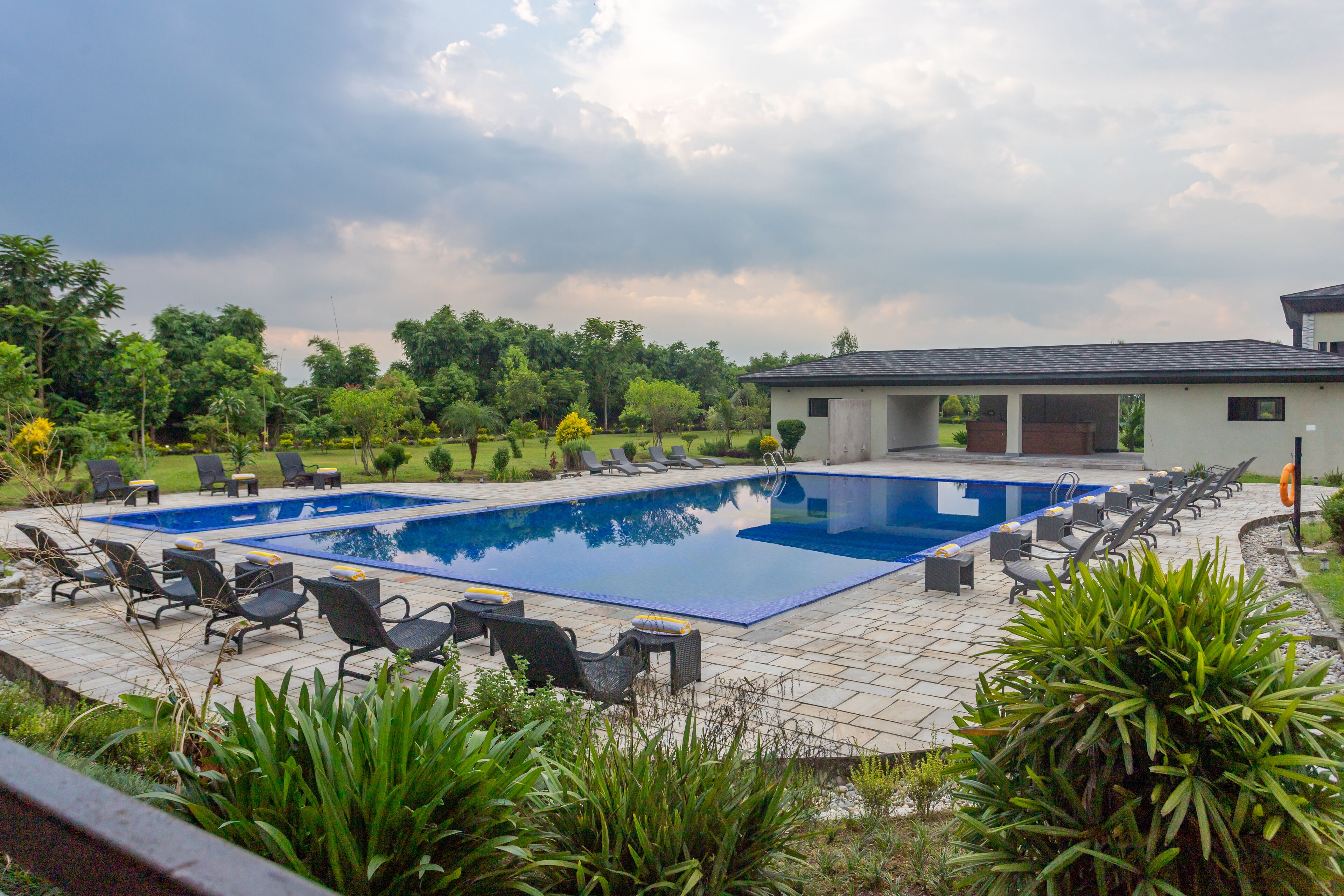 A rectangular swimming pool with a tiled deck, surrounded by lounge chairs and a small building with a sloped roof.