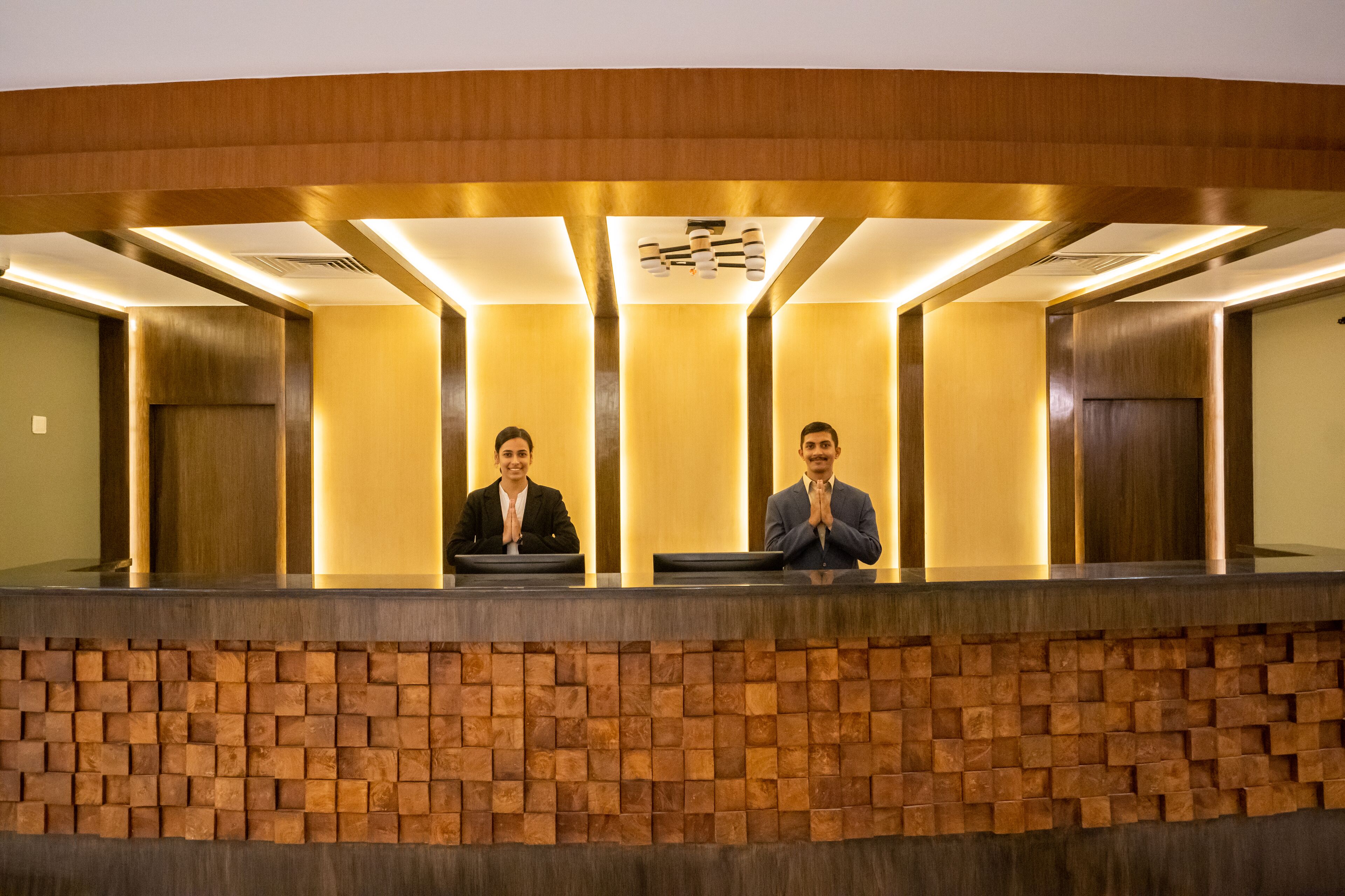 Una recepción con dos empleados, un diseño de pared de madera e iluminación empotrada en el techo.