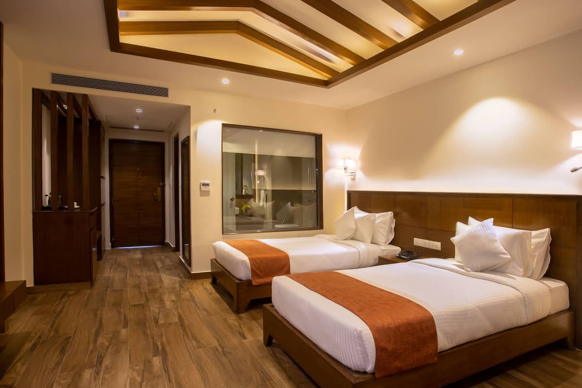 Habitación de hotel con dos camas, piso de madera, un espejo grande y techo de madera con iluminación empotrada.