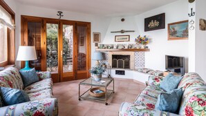 A living room with floral upholstery sofas, a glass coffee table, a fireplace, and a television. - Villa Mytilene II by Wonderful Italy (Cefalù)